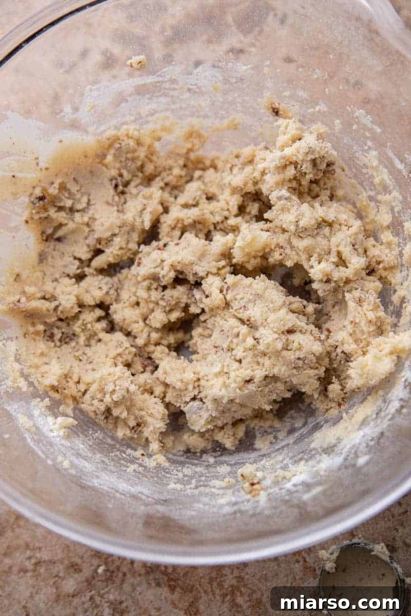 Melt-in-Your-Mouth Snowball Perfection 7 Pecan cookie dough in a mixing bowl after all ingredients are combined, showing the uniform distribution of chopped nuts.