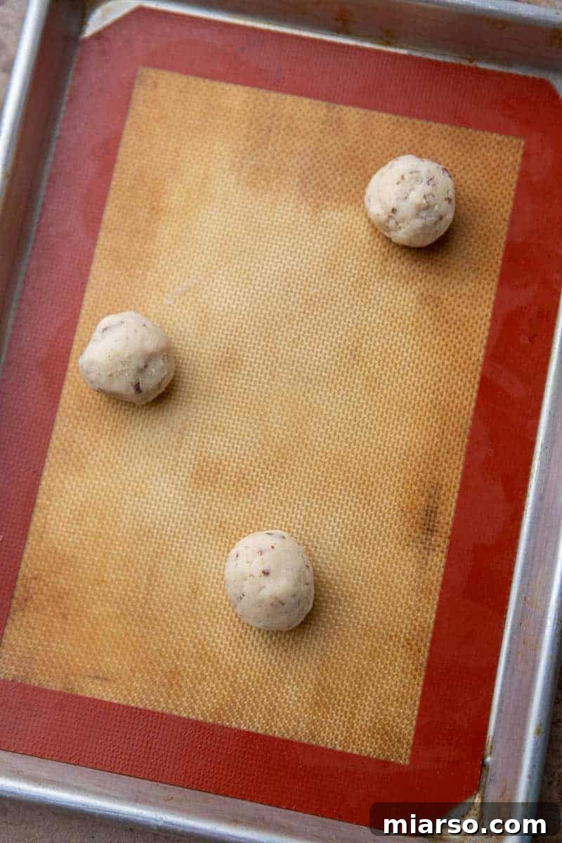 Melt-in-Your-Mouth Snowball Perfection 8 Uniformly shaped cookie dough balls placed on a parchment-lined baking sheet, ready for the oven.
