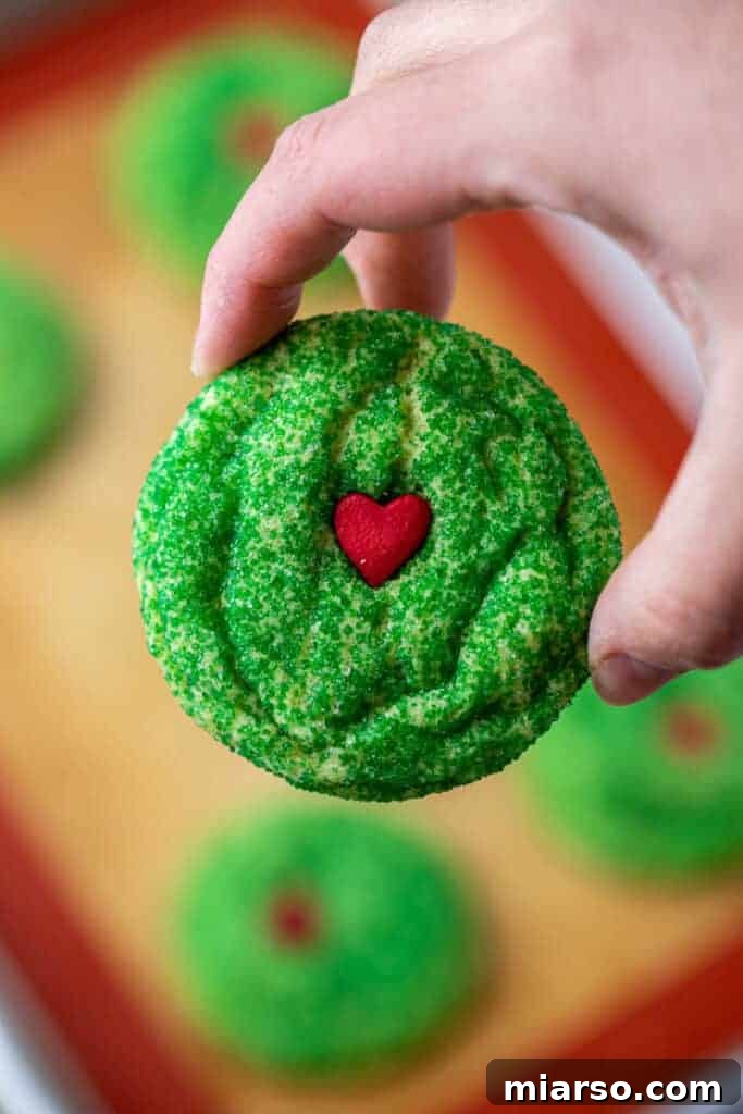 Grinch's Heart-Melting Sugar Cookies 5 Perfectly baked Grinch sugar cookies on a baking sheet, glowing green with red hearts