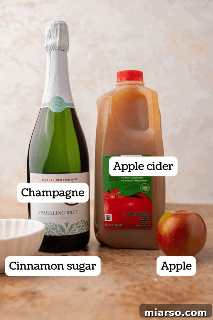 Sparkling 5-Minute Apple Cider Mimosas 3 Ingredients for apple cider mimosas laid out on a table, including apple cider, champagne, cinnamon, sugar, and apples.