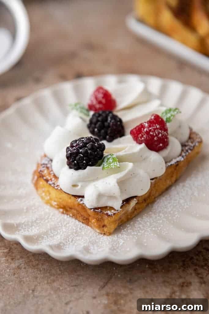 The Ultimate Brioche French Toast 8 A stack of brioche French toast generously topped with whipped cream, fresh raspberries, and blueberries