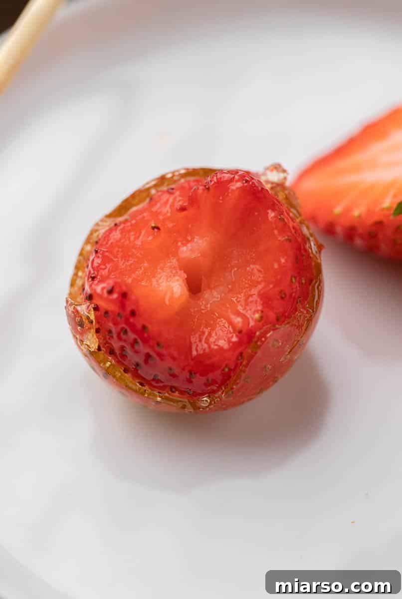Candy coated strawberries with a bite taken out of them, showing the crisp sugar shell and juicy interior.