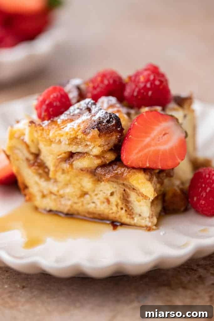 A slice of brioche French toast casserole on a plate, garnished with powdered sugar and berries.