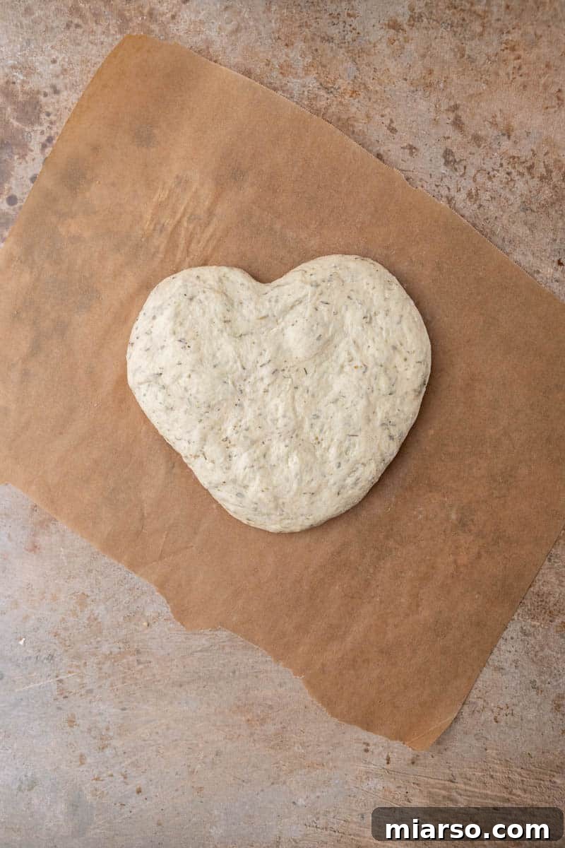 Pizza dough being gently shaped into a heart on parchment paper