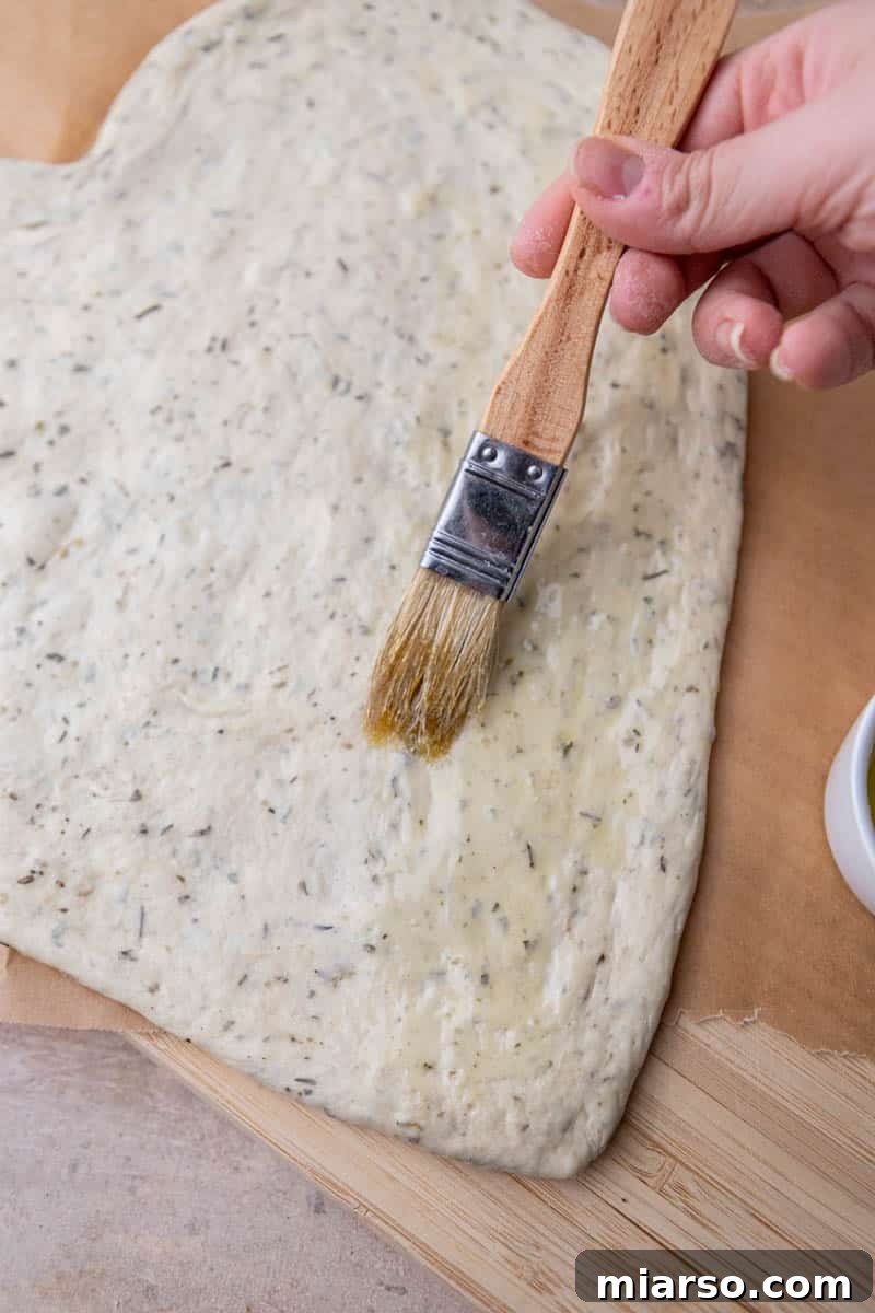 Brushing olive oil onto the edges of heart-shaped pizza dough for a crispy crust