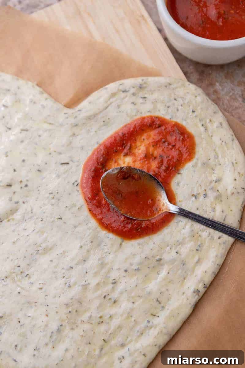 Spreading rich tomato sauce evenly over the heart-shaped pizza dough