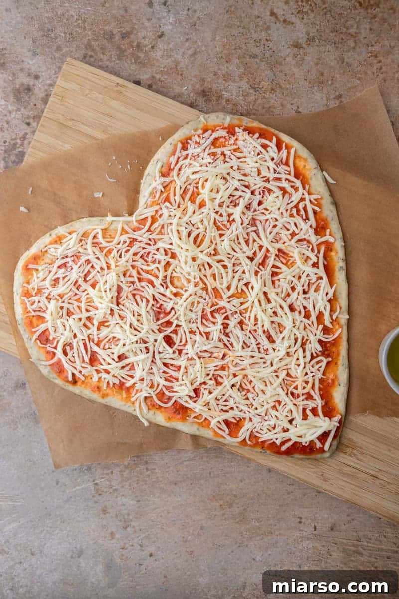 Generously adding shredded cheese onto the heart-shaped pizza base