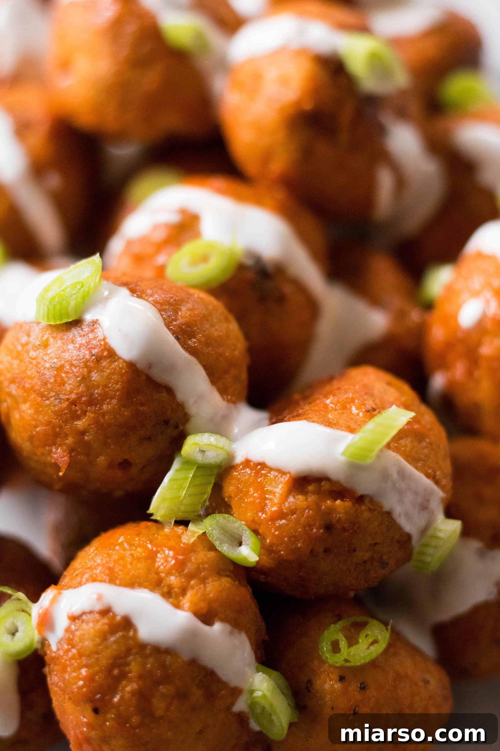 Chicken buffalo meatballs generously coated with ranch dressing and sprinkled with fresh green onions.
