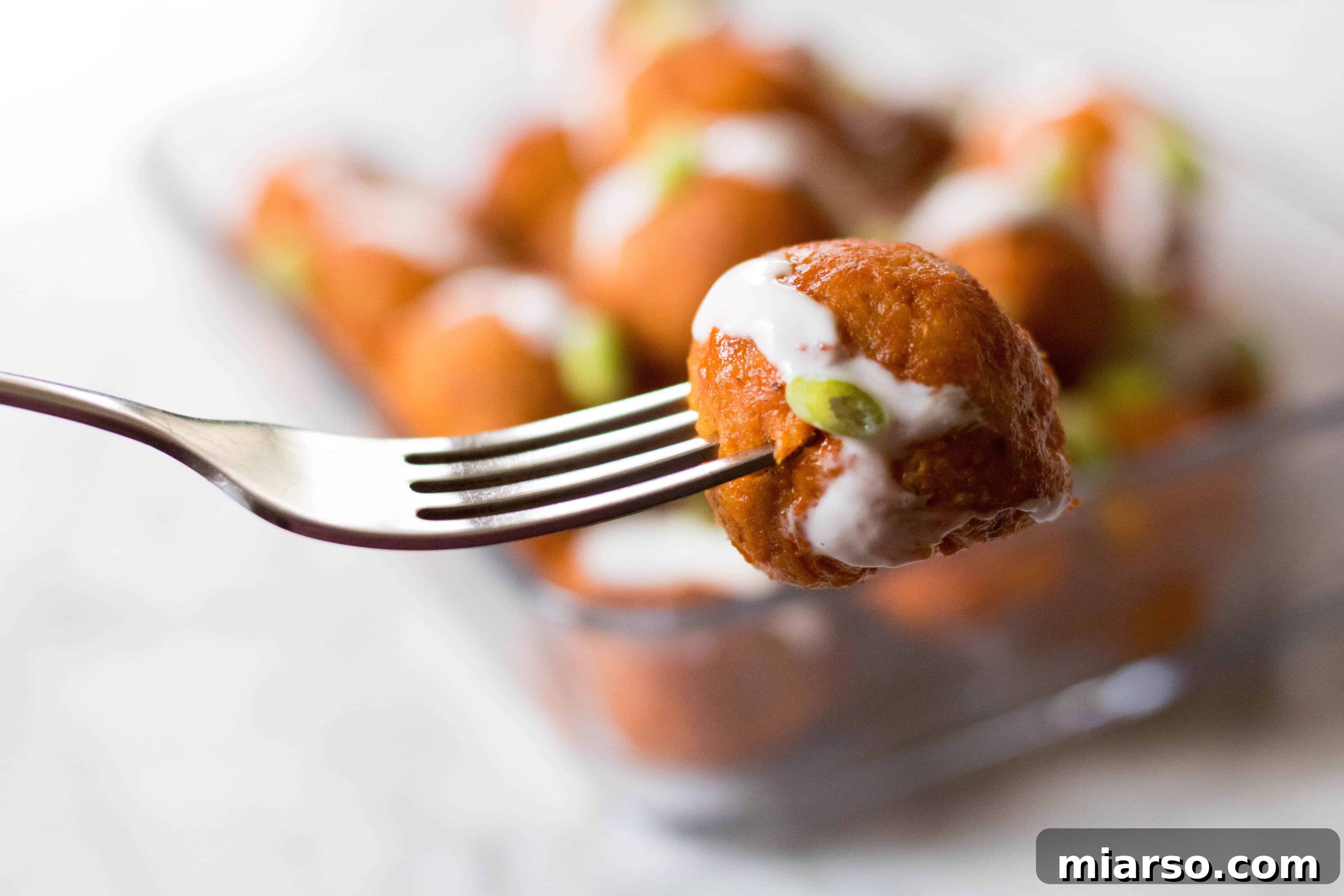 A fork piercing a healthy baked buffalo chicken meatball, ready to be enjoyed.