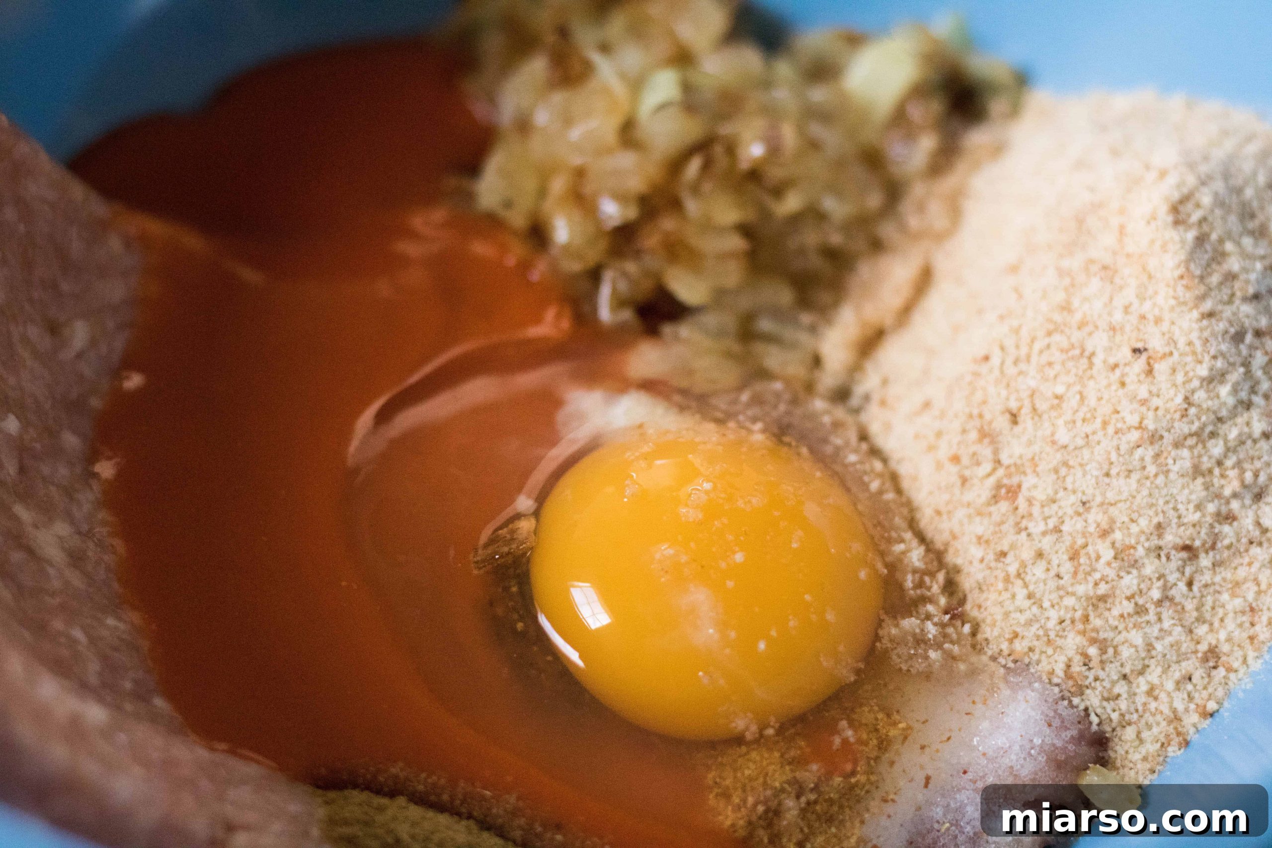 Bowl with ground chicken, various spices, breadcrumbs, and egg, ready for mixing.