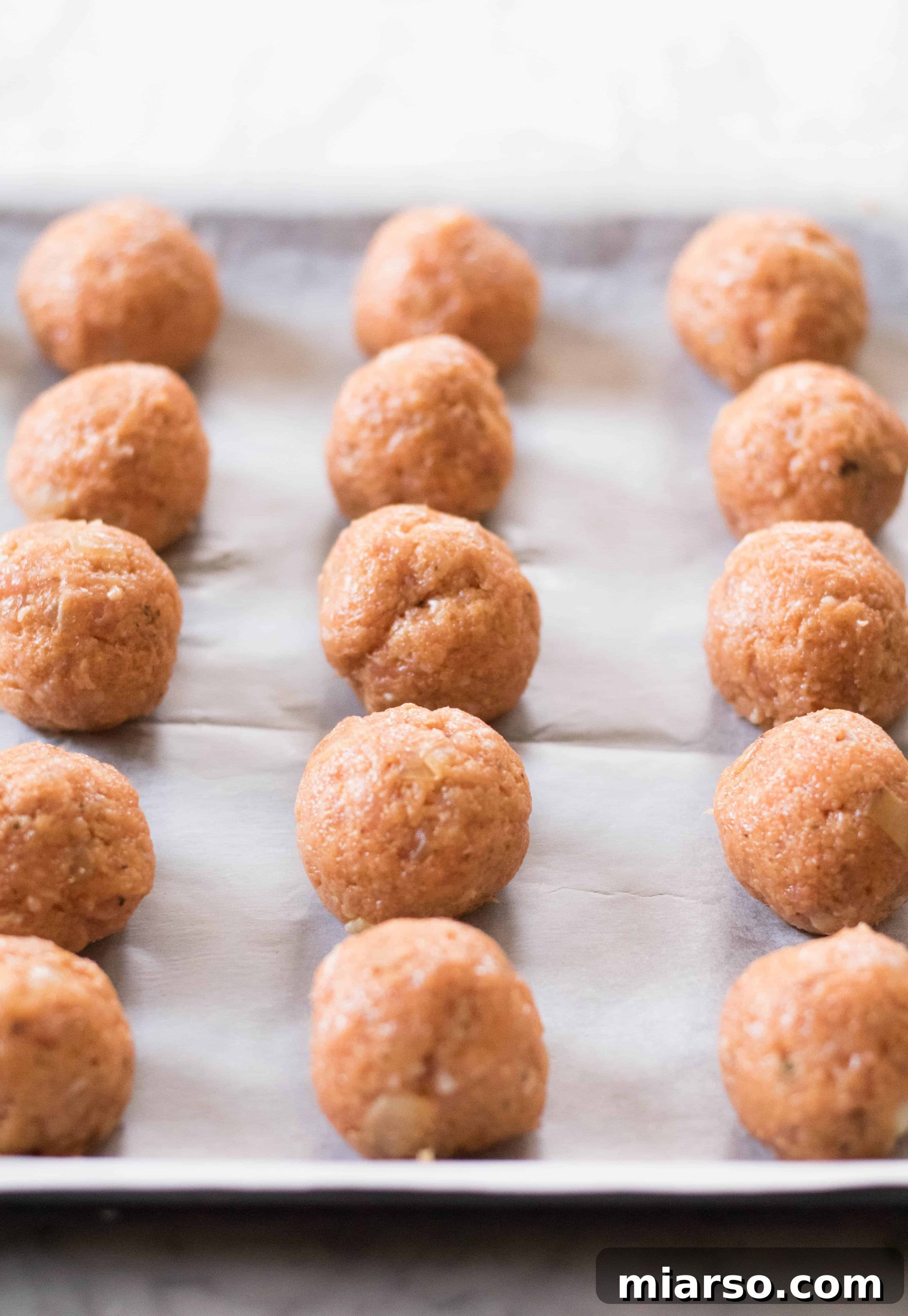 Buffalo chicken meatballs neatly arranged on a parchment-lined baking sheet, ready for baking.