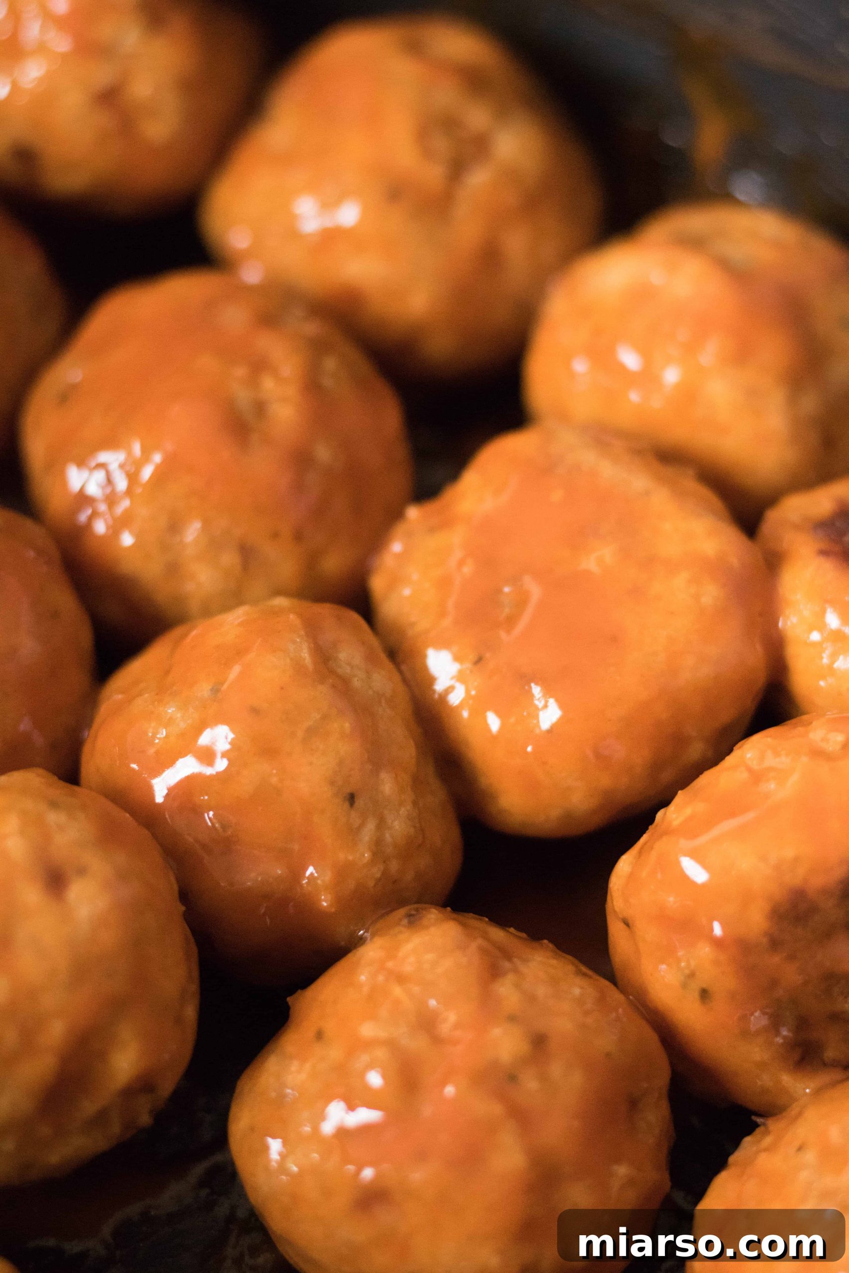 Baked chicken meatballs coated in a glossy, vibrant buffalo sauce, ready to be served.