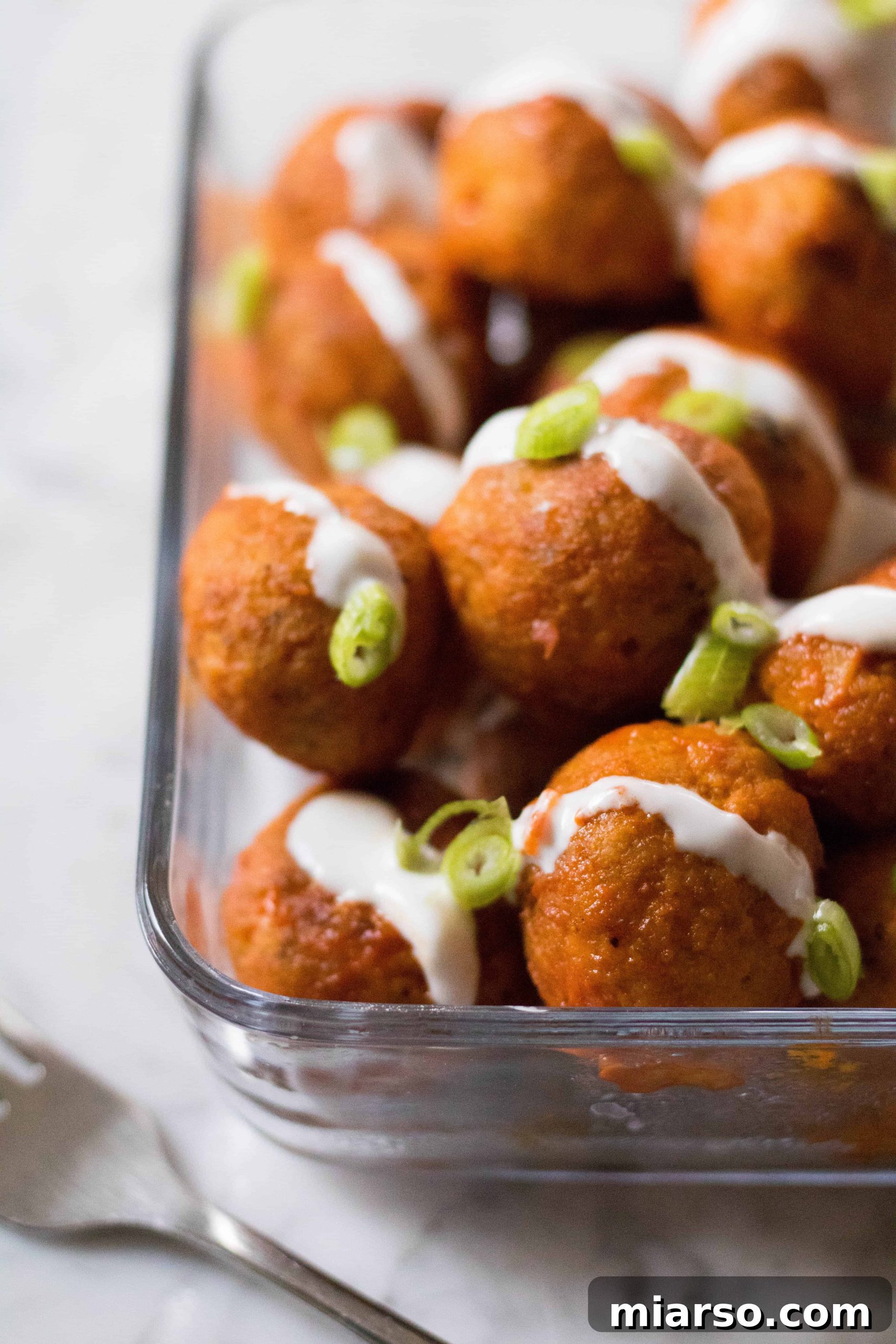 A bowl of freshly glazed buffalo chicken meatballs, steaming and ready to eat.