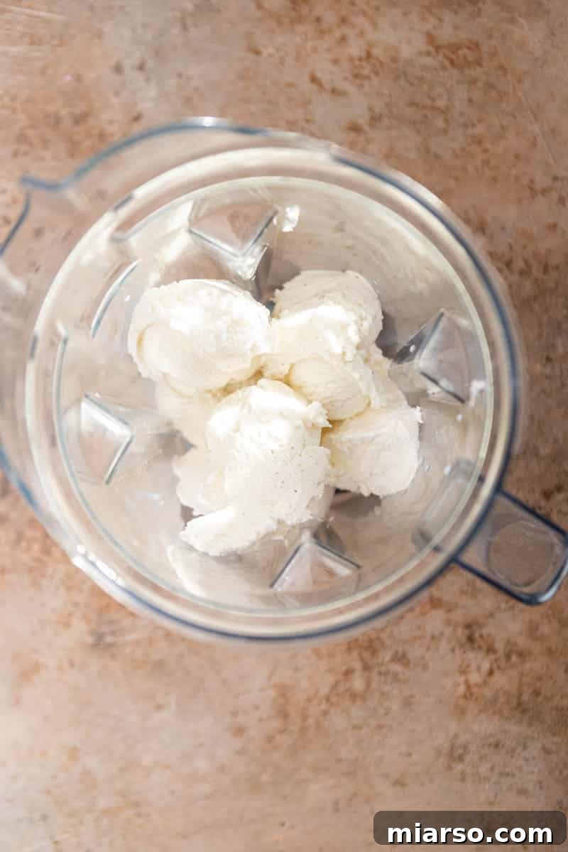 Vanilla ice cream, milk, and cool whip being added to a blender cup.