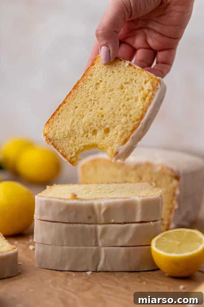 A hand holding a slice of a perfectly baked Starbucks lemon loaf cake with thick glaze.