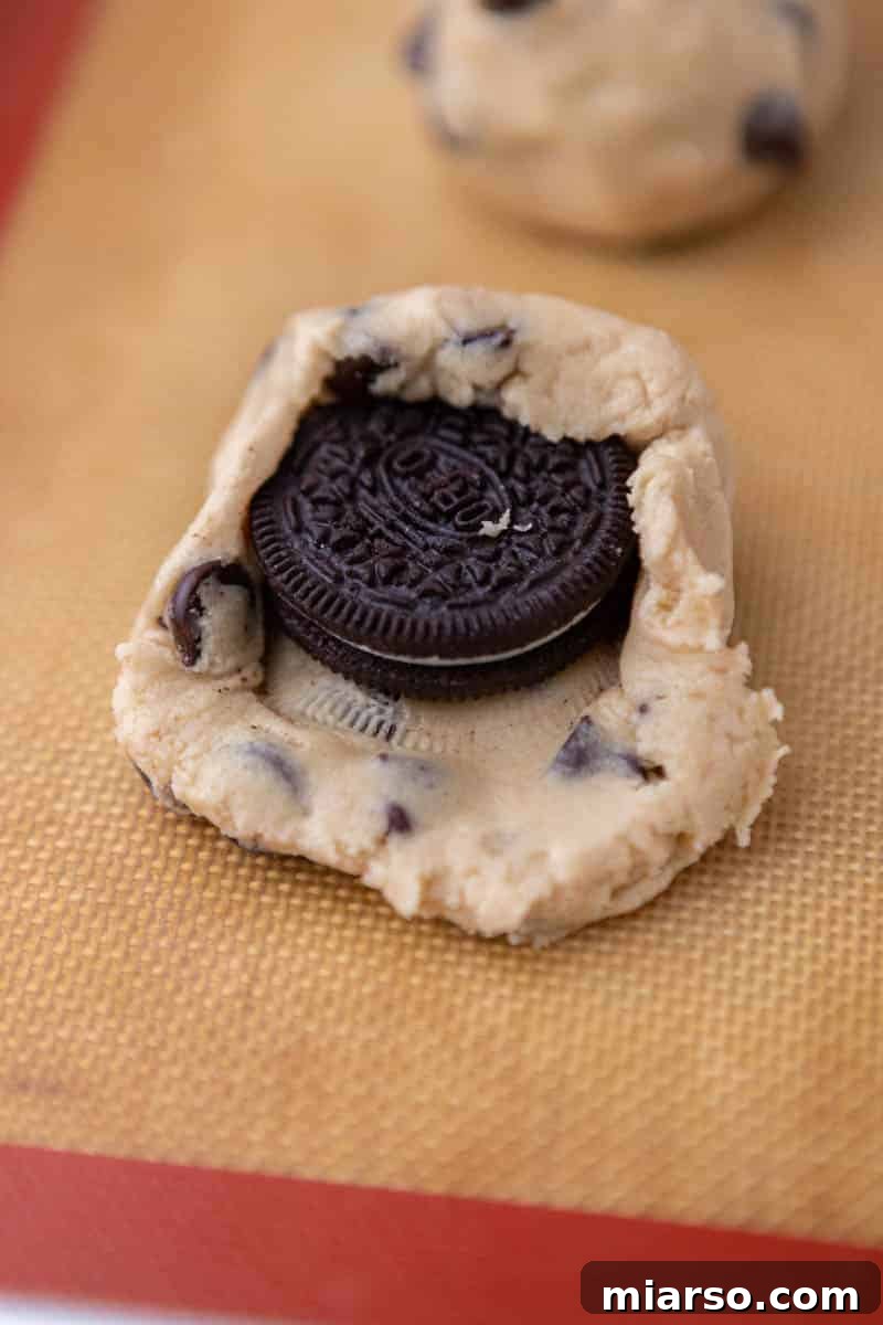 Oreo Stuffed Chocolate Chip Cookies Made Simple 8 An Oreo cookie carefully placed in the center of a flattened disc of chocolate chip cookie dough, ready for stuffing.