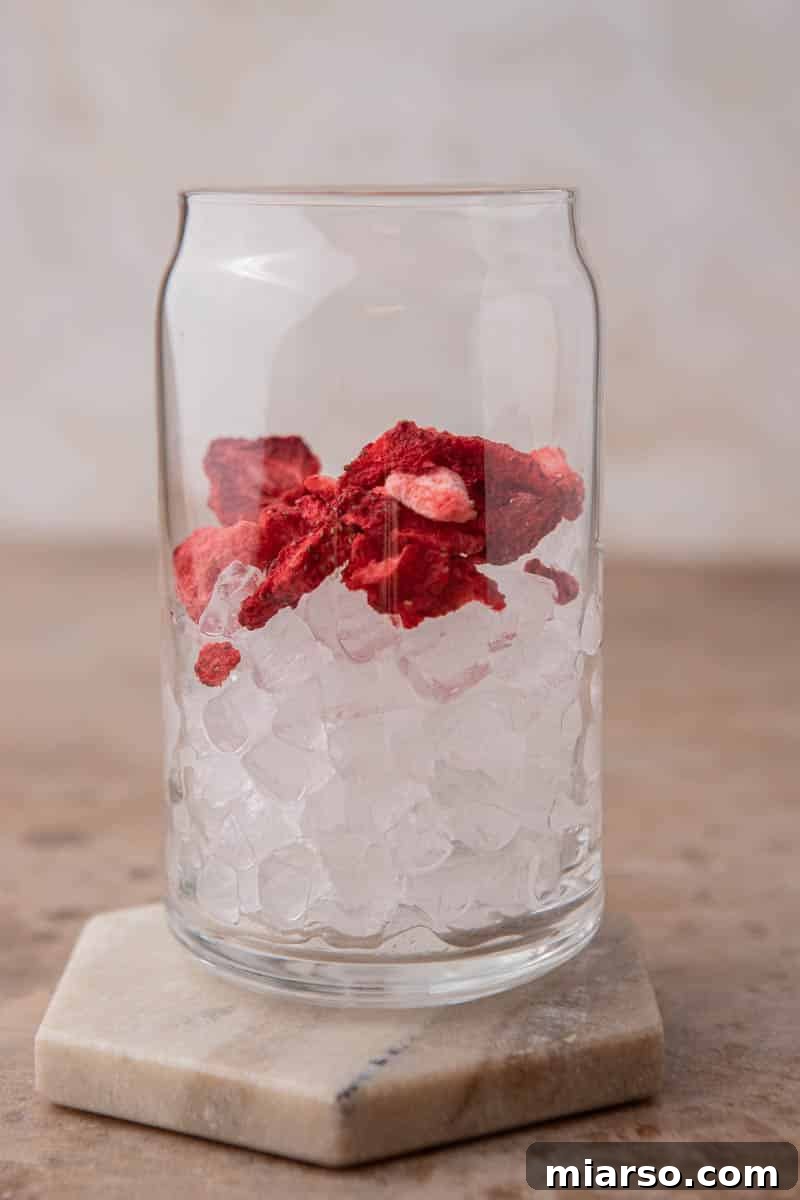 Craft Your Own Starbucks Strawberry Acai Refresher 6 Glass being filled with ice and freeze-dried strawberries