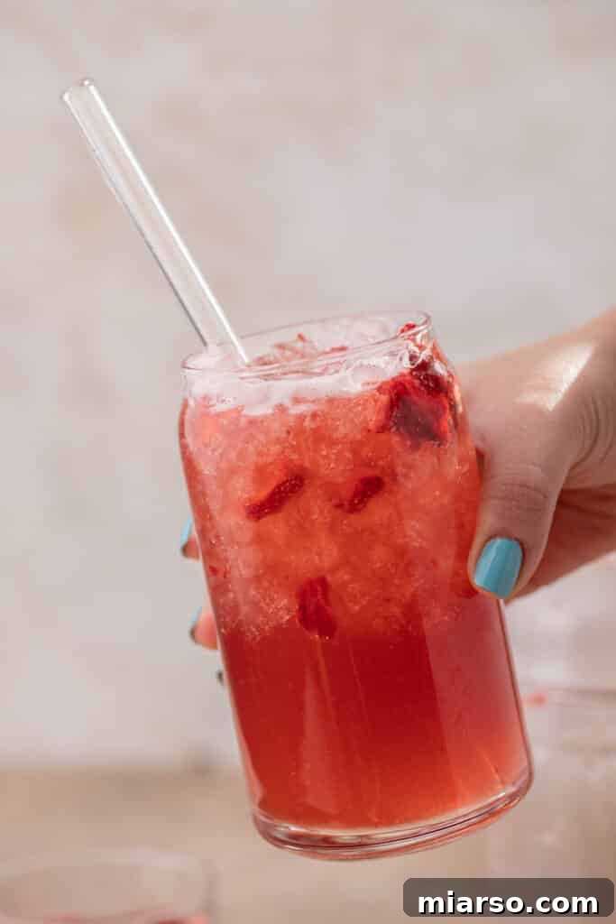 Craft Your Own Starbucks Strawberry Acai Refresher 8 Hand holding a glass of homemade Starbucks strawberry acai refresher