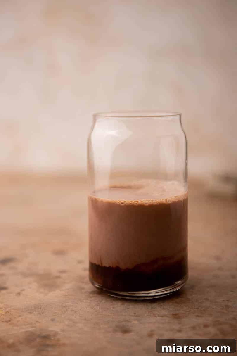 Chocolate syrup being poured into a glass with espresso, ready for mixing to create an iced mocha.