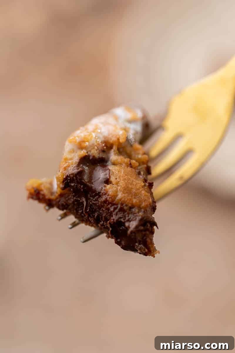 Gooey Skillet Chocolate Chip Pizookie 12 A fork taking a bite from a warm chocolate chip cookie in a skillet, showcasing the melted chocolate.