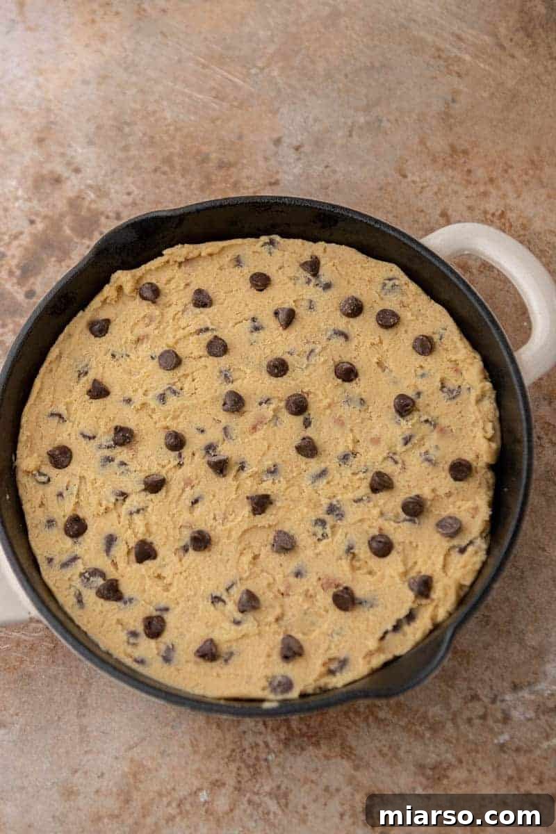 Gooey Skillet Chocolate Chip Pizookie 7 Chocolate chip cookie dough pressed evenly into a cast iron skillet, with extra chocolate chips sprinkled on top.