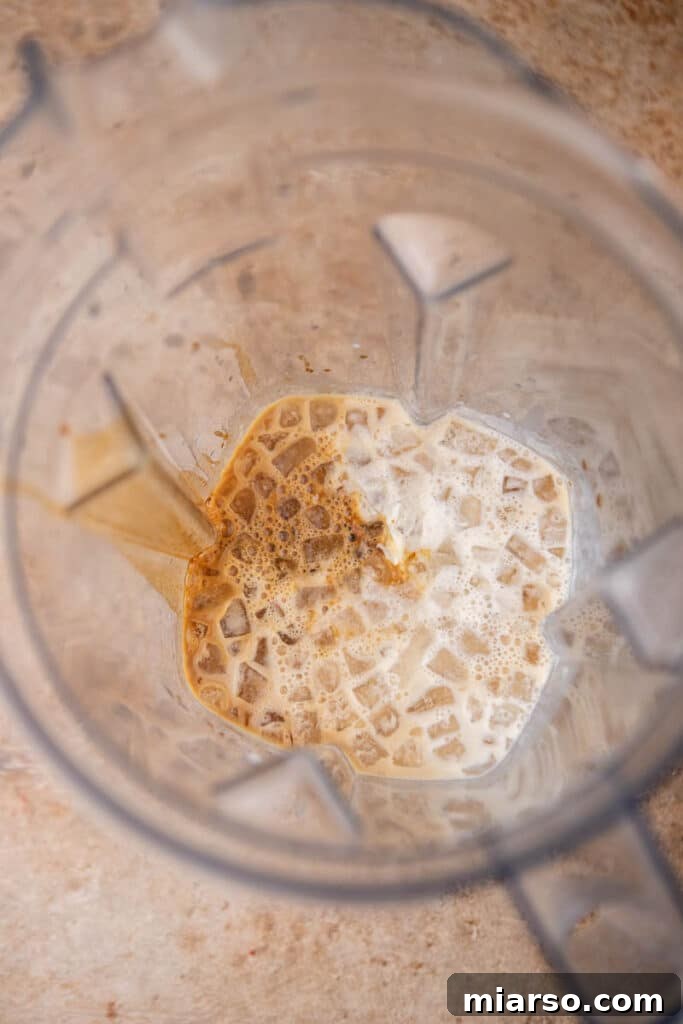 Ingredients for homemade McDonald’s caramel frappe including ice, coffee, caramel syrup, and milk in a blender before blending