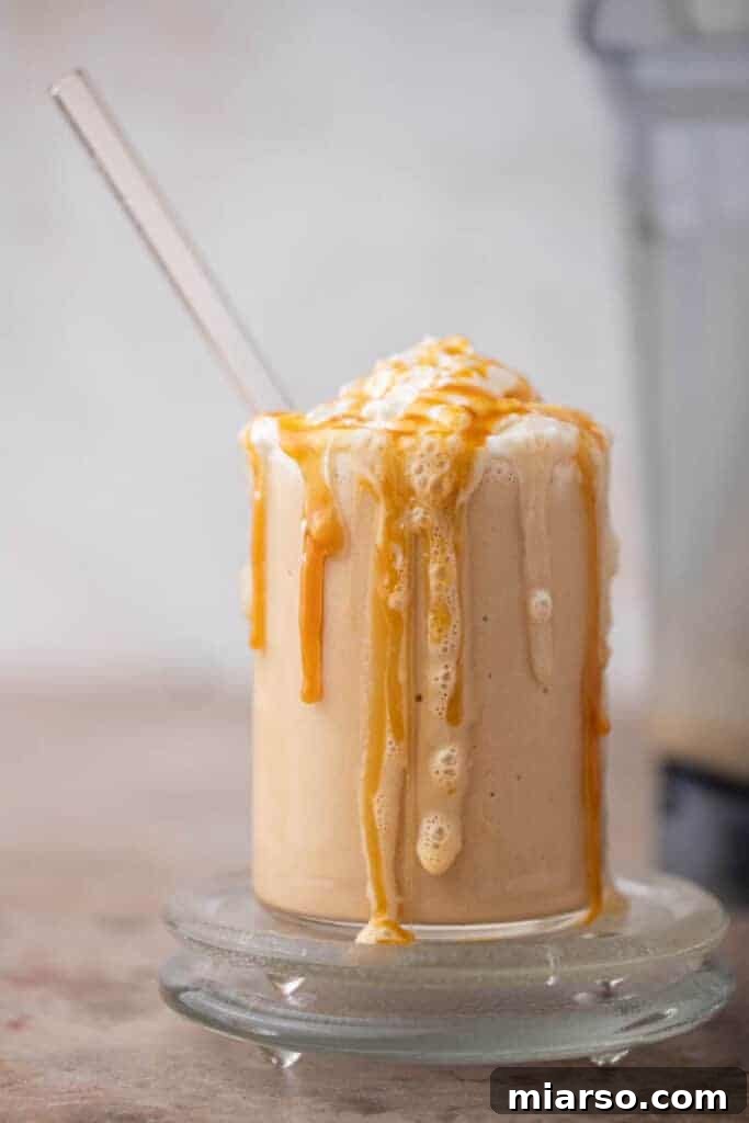 Thick caramel frappe in a glass overflowing with whipped cream and caramel drizzle