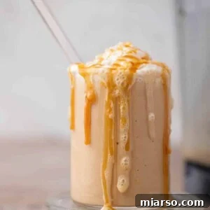 Thick caramel frappe in a glass overflowing with whipped cream and caramel drizzle