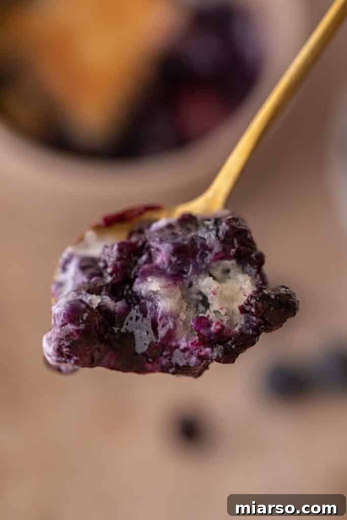 Irresistible Homemade Blueberry Cobbler 10 A spoon scooping a generous portion of warm blueberry cobbler from a larger dish, showing the juicy fruit and tender topping.