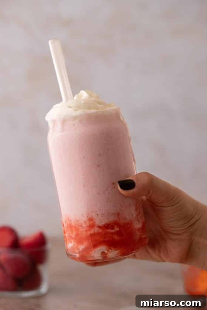 Hand holding copycat Starbucks strawberry creme frappuccino, showcasing the vibrant pink color and whipped cream topping.