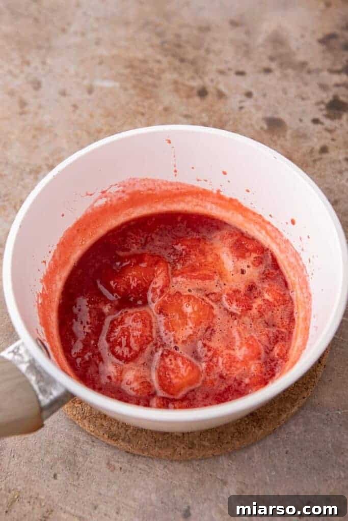 Strawberry sauce reducing and mashing in a pan, showing its developing thickness.
