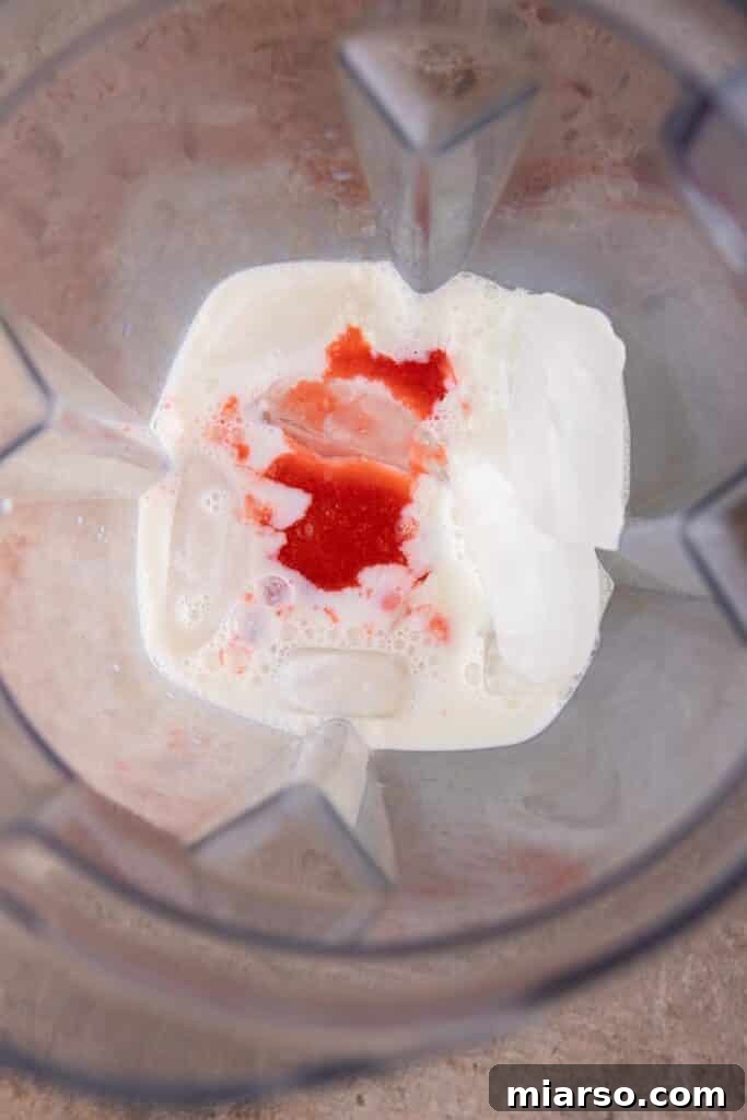 Ice, milk, and strawberry puree added to a blender, ready to be processed.