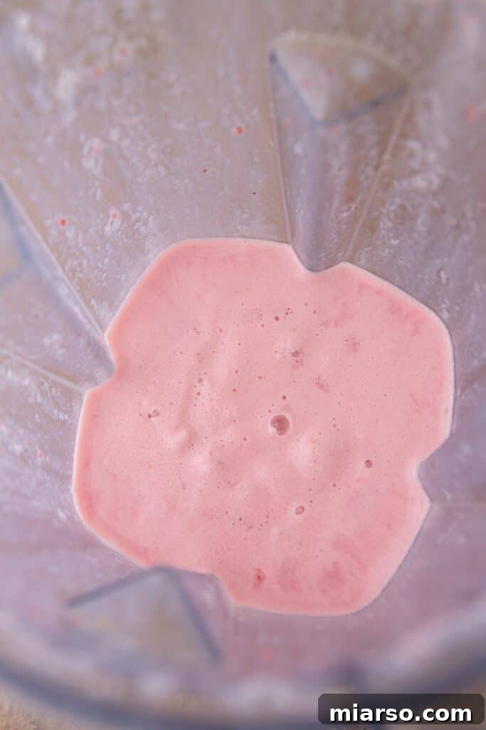 Freshly blended strawberry frappuccino pouring into a glass, showing its creamy texture.