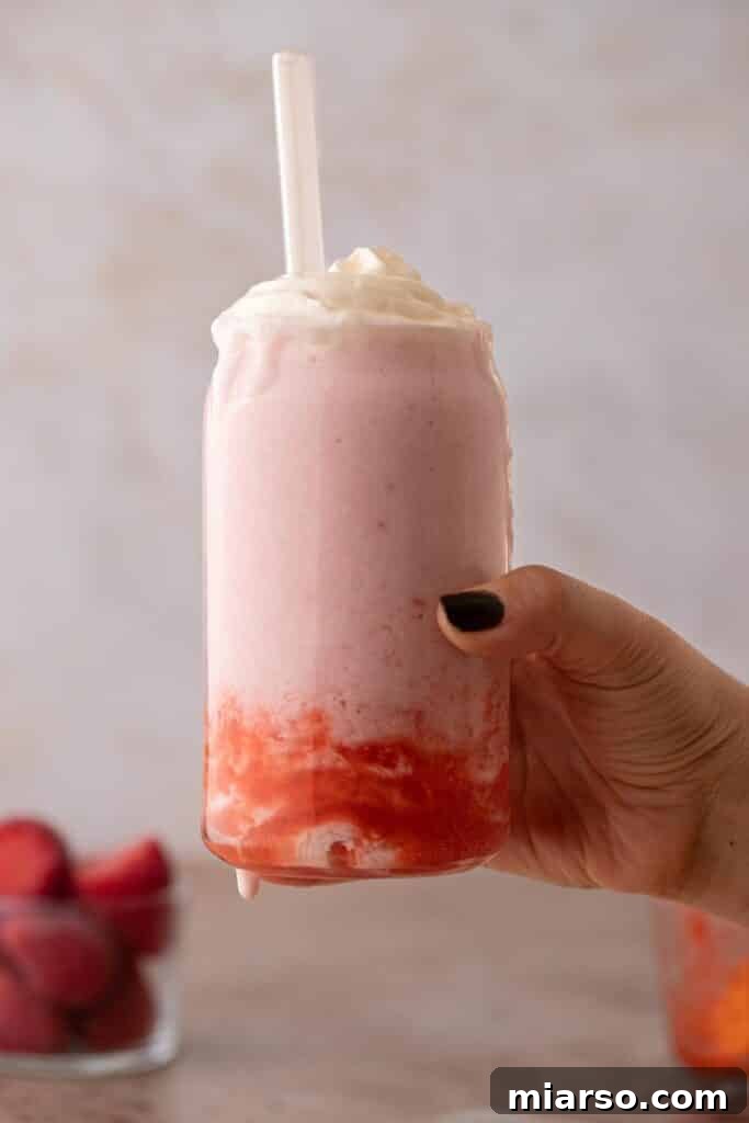 Finished Strawberry Frappuccino in a glass with whipped cream and strawberry drizzle, ready to be enjoyed.