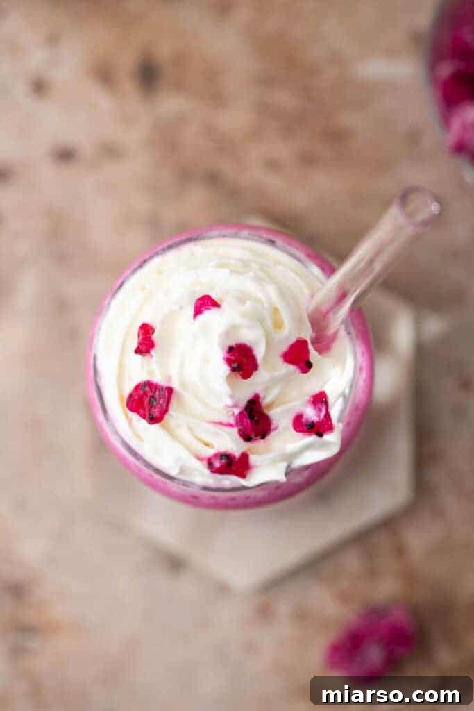 Overhead shot of a pink Barbie Frappuccino in a tall glass, garnished with whipped cream and dragon fruit.