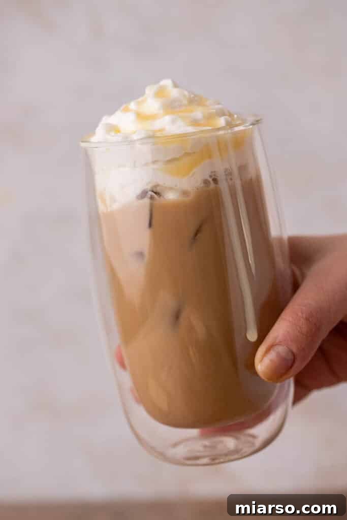 Hand holding a glass of iced Starbucks white chocolate mocha, showing whipped cream and white chocolate drizzle.