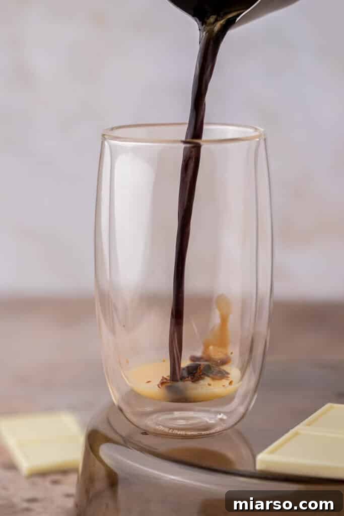 Freshly brewed espresso being poured into a glass with white chocolate sauce