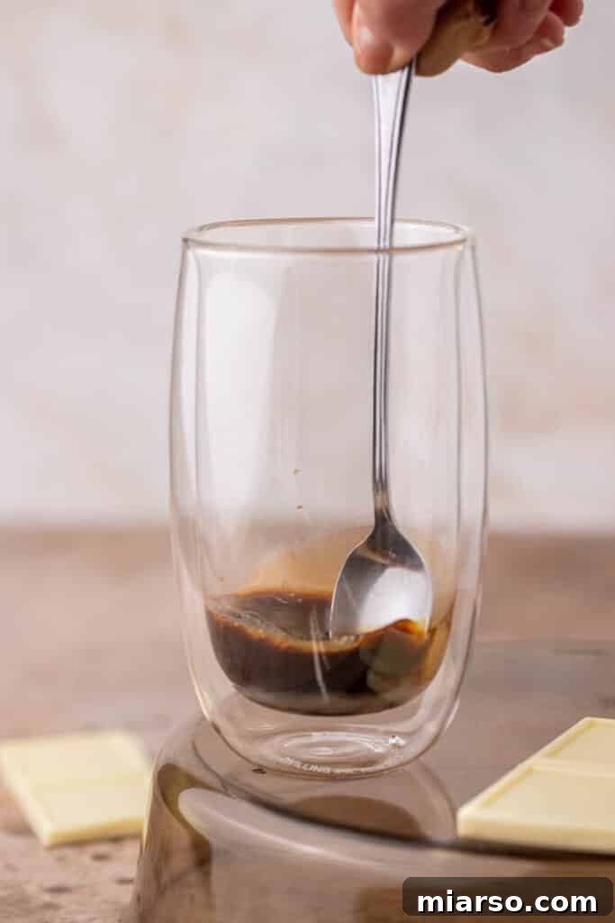 Spoon stirring white chocolate sauce and espresso in a glass