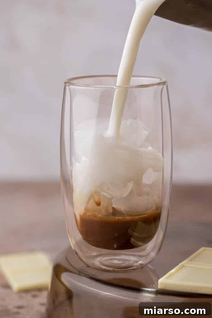 Milk being poured into a glass with ice, espresso, and white chocolate