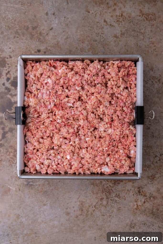 Strawberry rice krispies mixture pressed into a prepared pan.