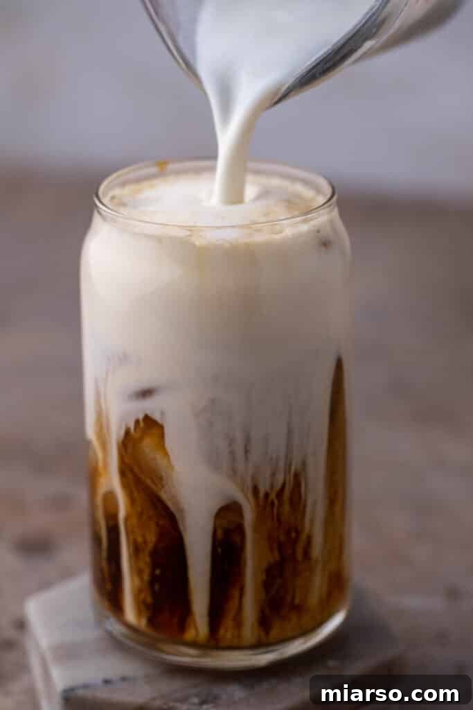 Pouring the frothy vanilla sweet cream cold foam on top of cold brew coffee