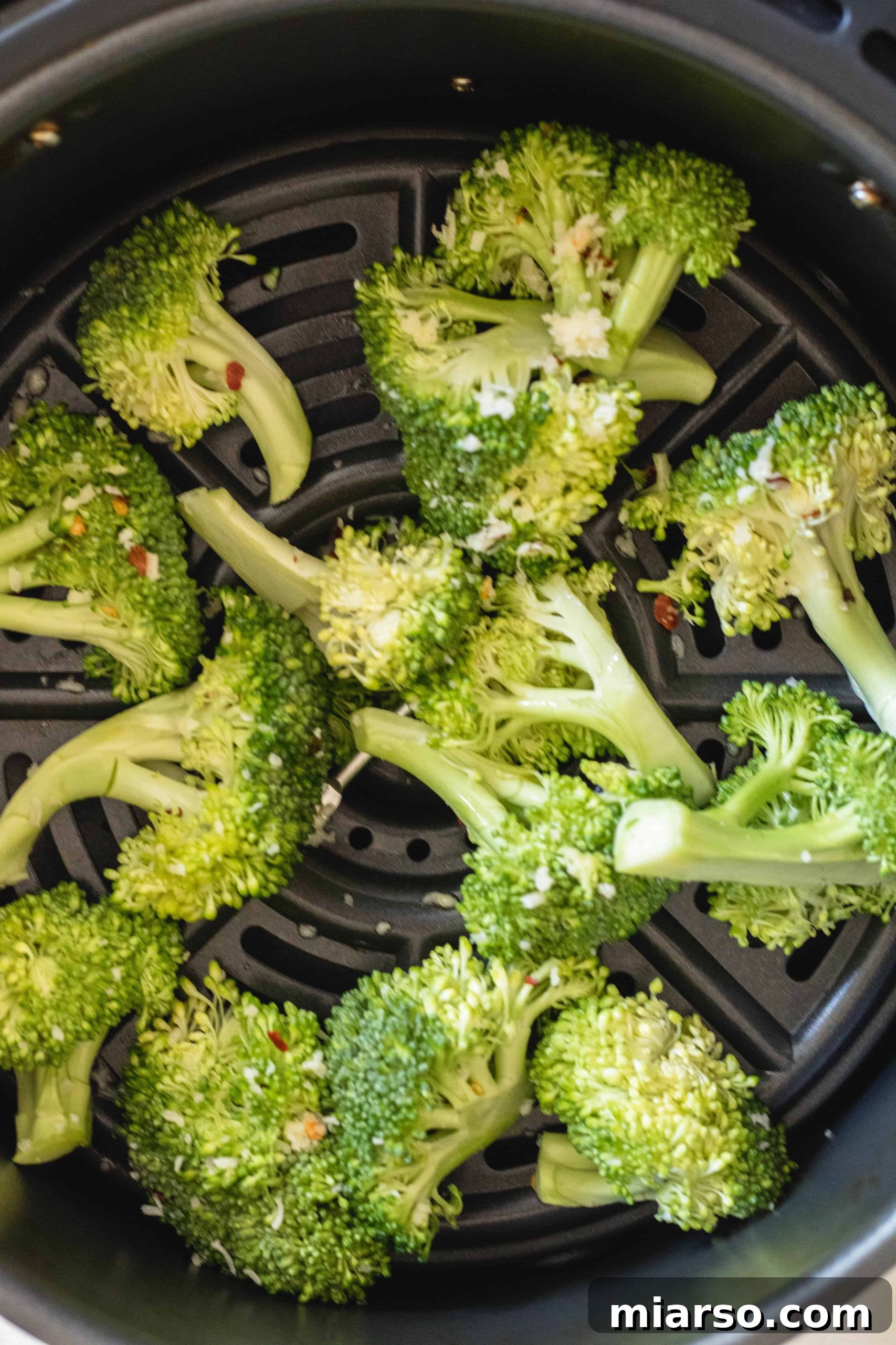 Air fryer easy broccoli recipe, showing seasoned broccoli in the air fryer basket