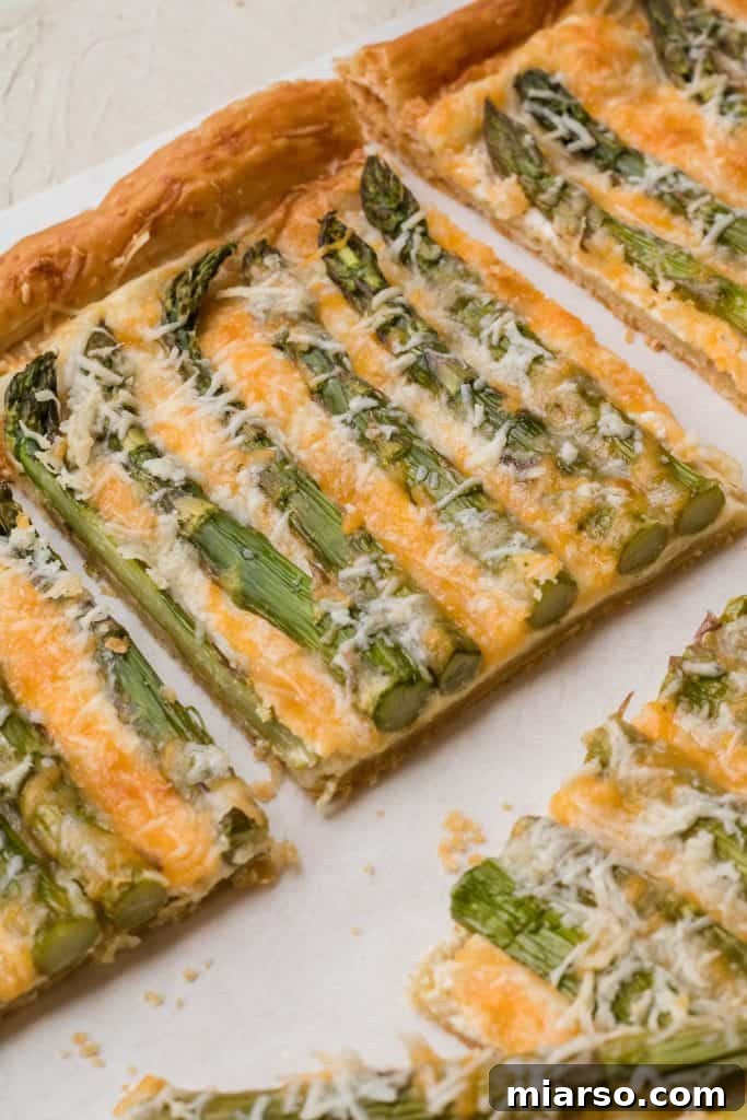 An artistic asparagus tart made with puff pastry, fresh asparagus, and cheese.