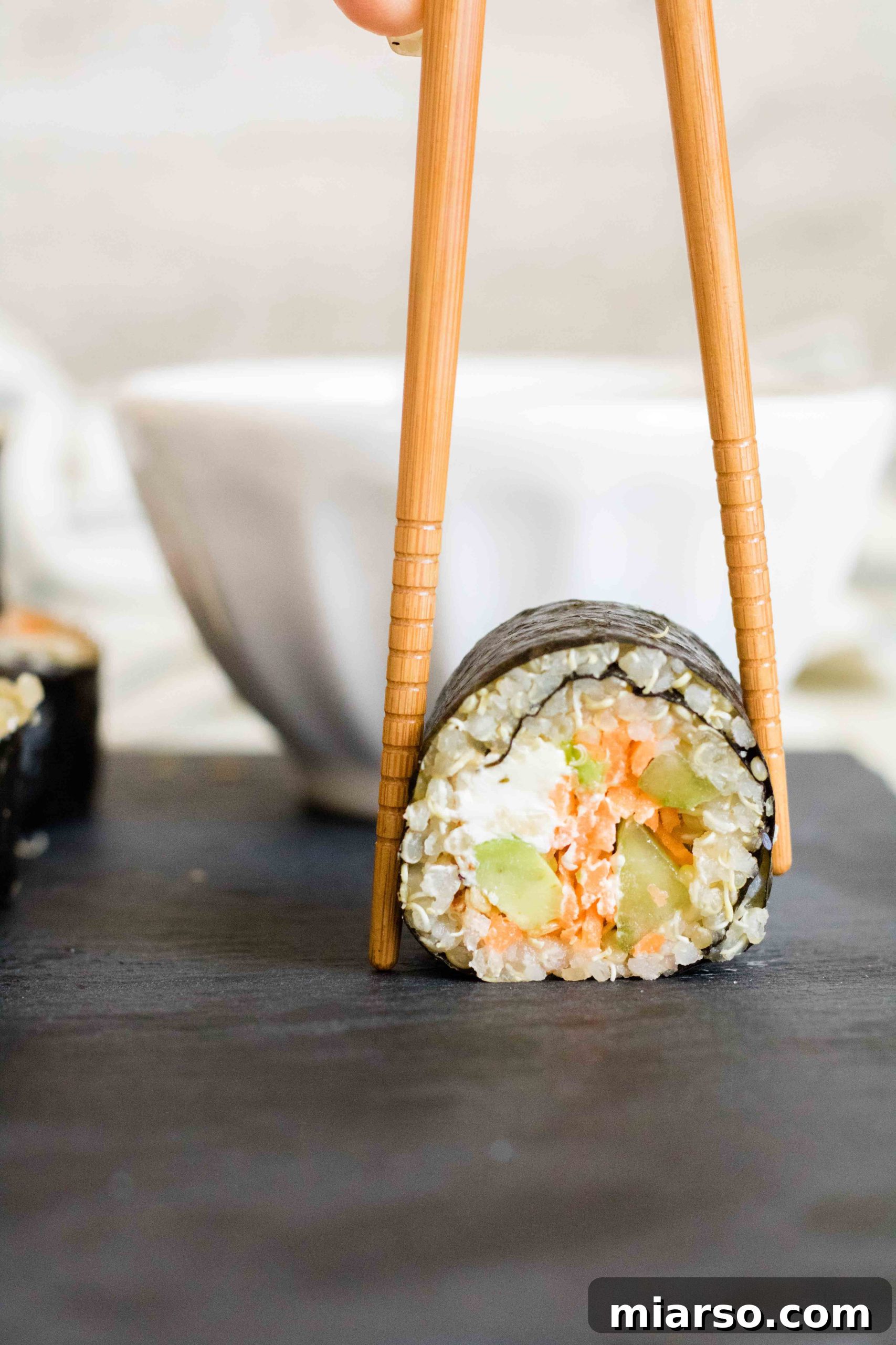 Hand making quinoa sushi, showing the process of spreading quinoa on nori.