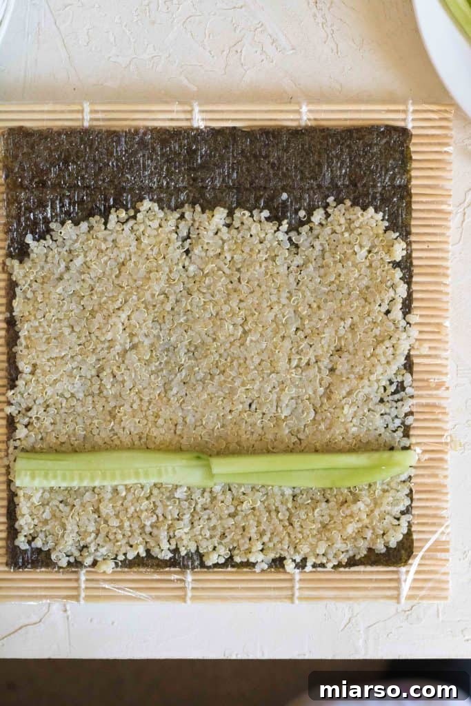 Arranging cucumber matchsticks on the quinoa-covered nori sheet.