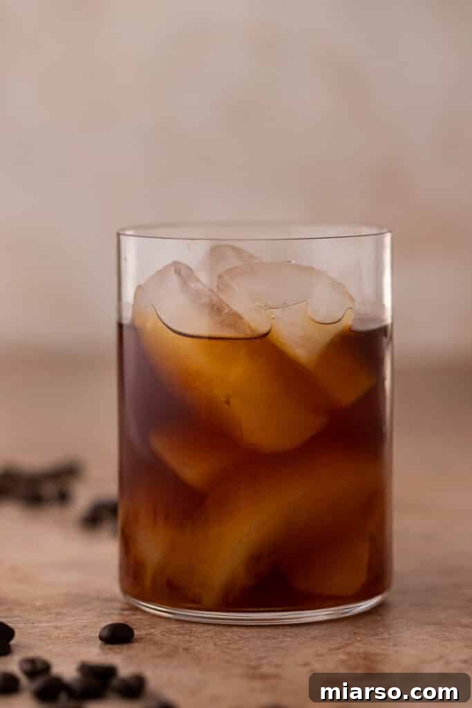 Pouring cold brew over ice in a tall glass, a key stage in preparing Emma Chamberlain's cold brew.
