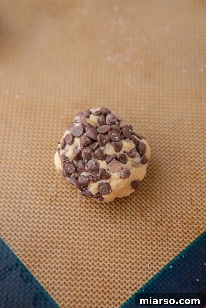 Cookie dough ball coated in mini chocolate chips, ready for baking.