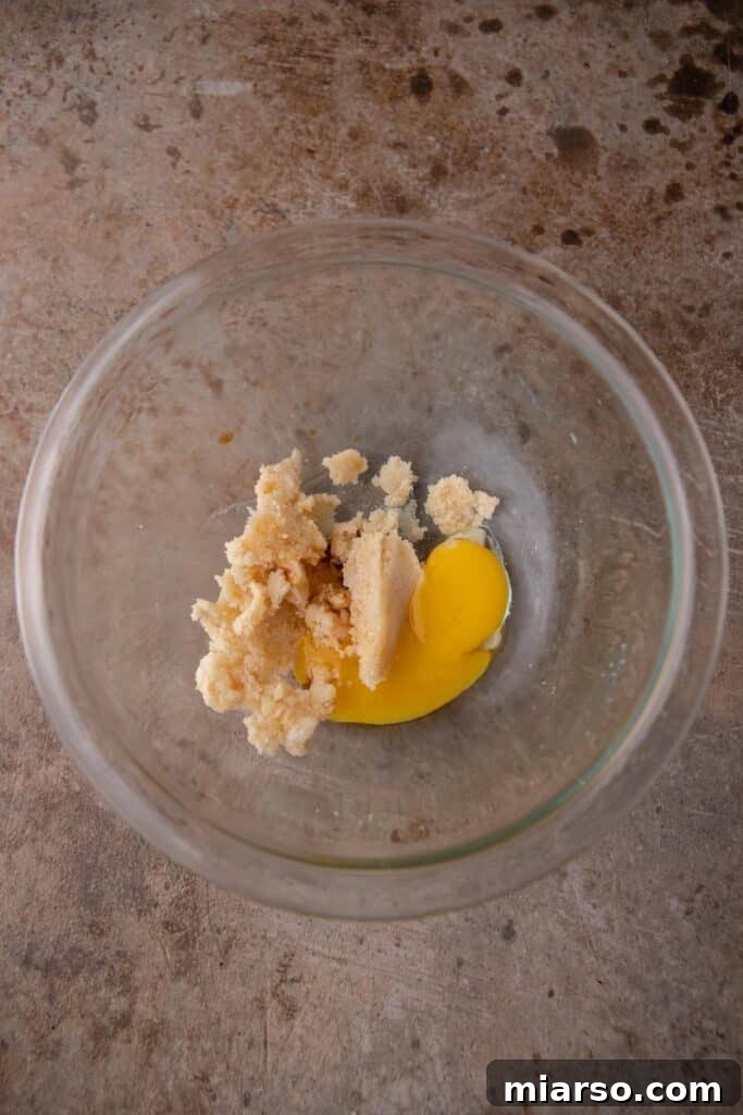 Wet ingredients (butter, sugars, vanilla, egg yolk) being creamed together in a bowl for double chocolate cookie dough.