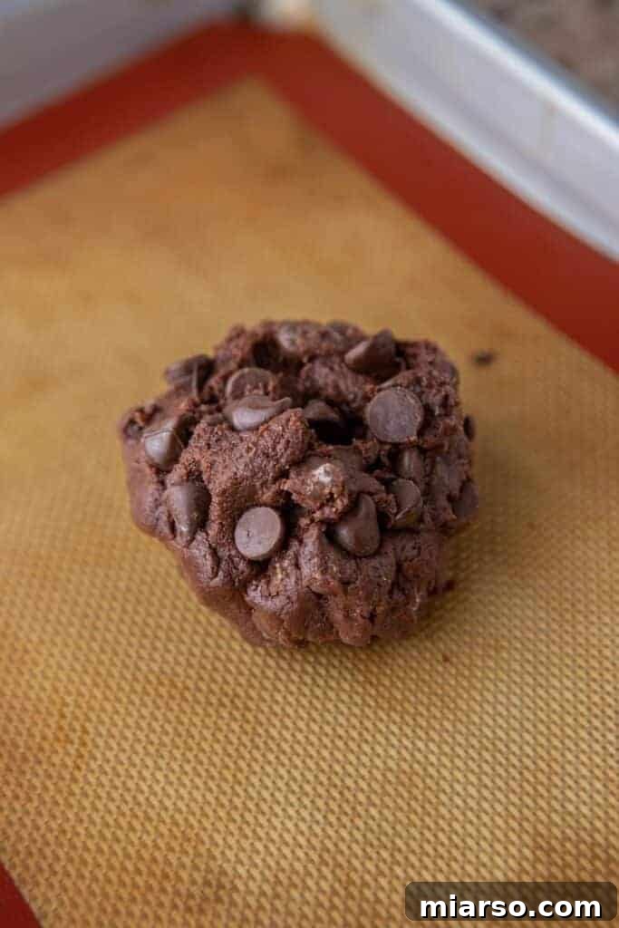 A single mound of double chocolate cookie dough placed on a parchment-lined baking sheet, topped with extra chocolate chips.