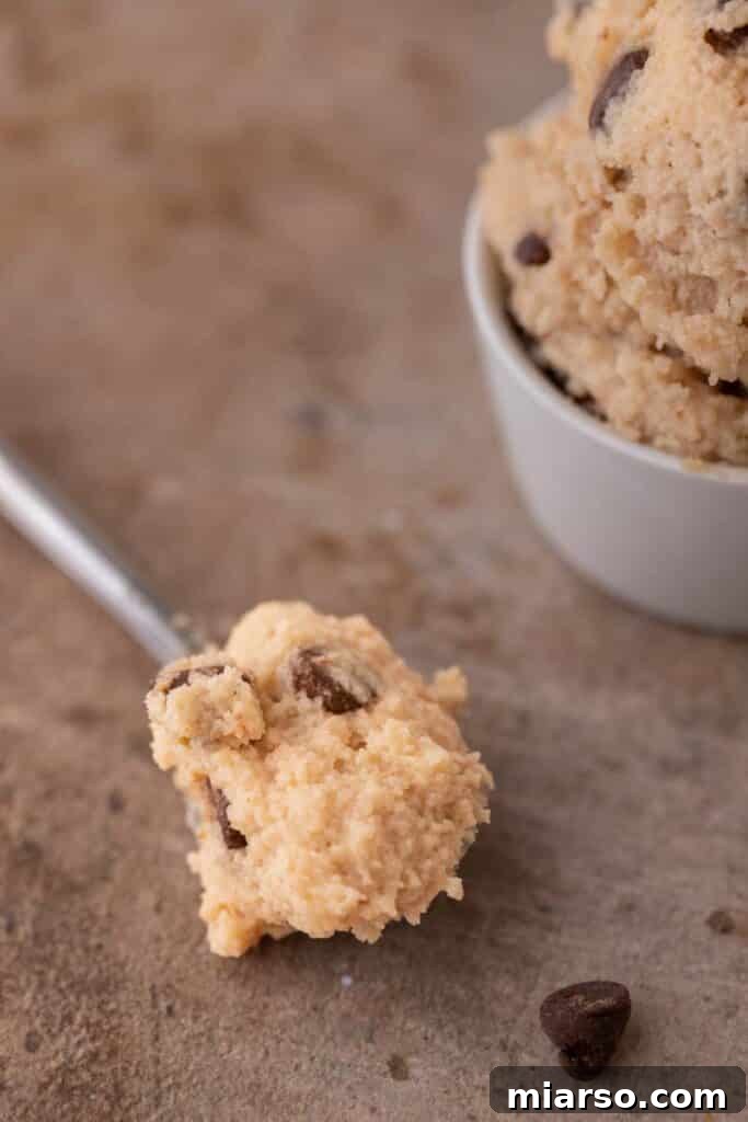 A spoon scooping a portion of edible cottage cheese cookie dough from a bowl.